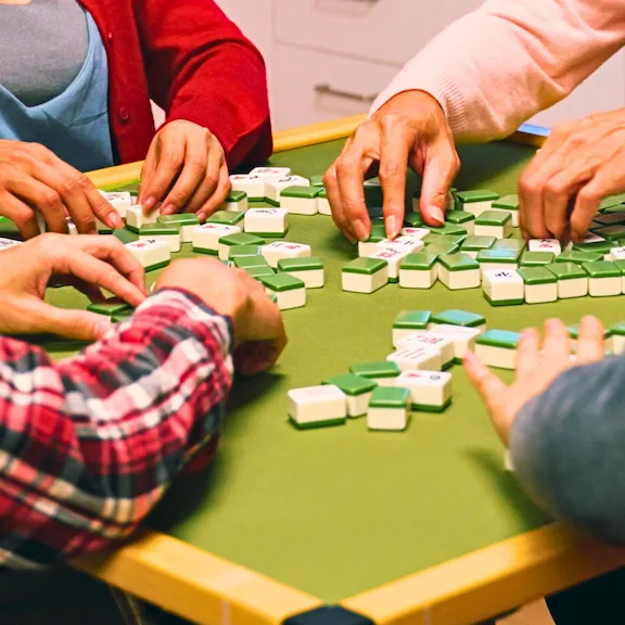 Four people's hands arranging Mahjong tiles